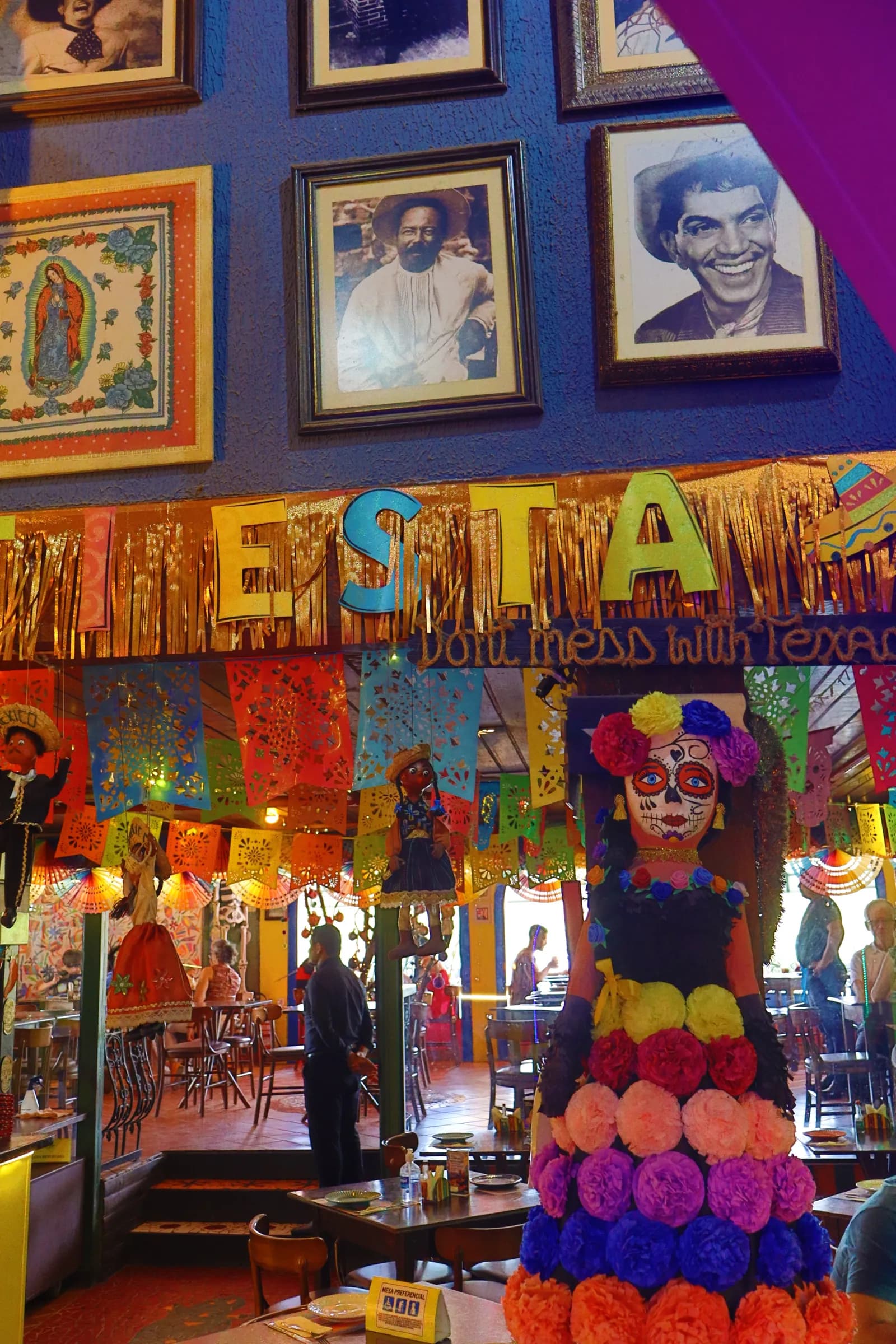 Salão movimentado com faixa "fiesta", papel picado e catrina