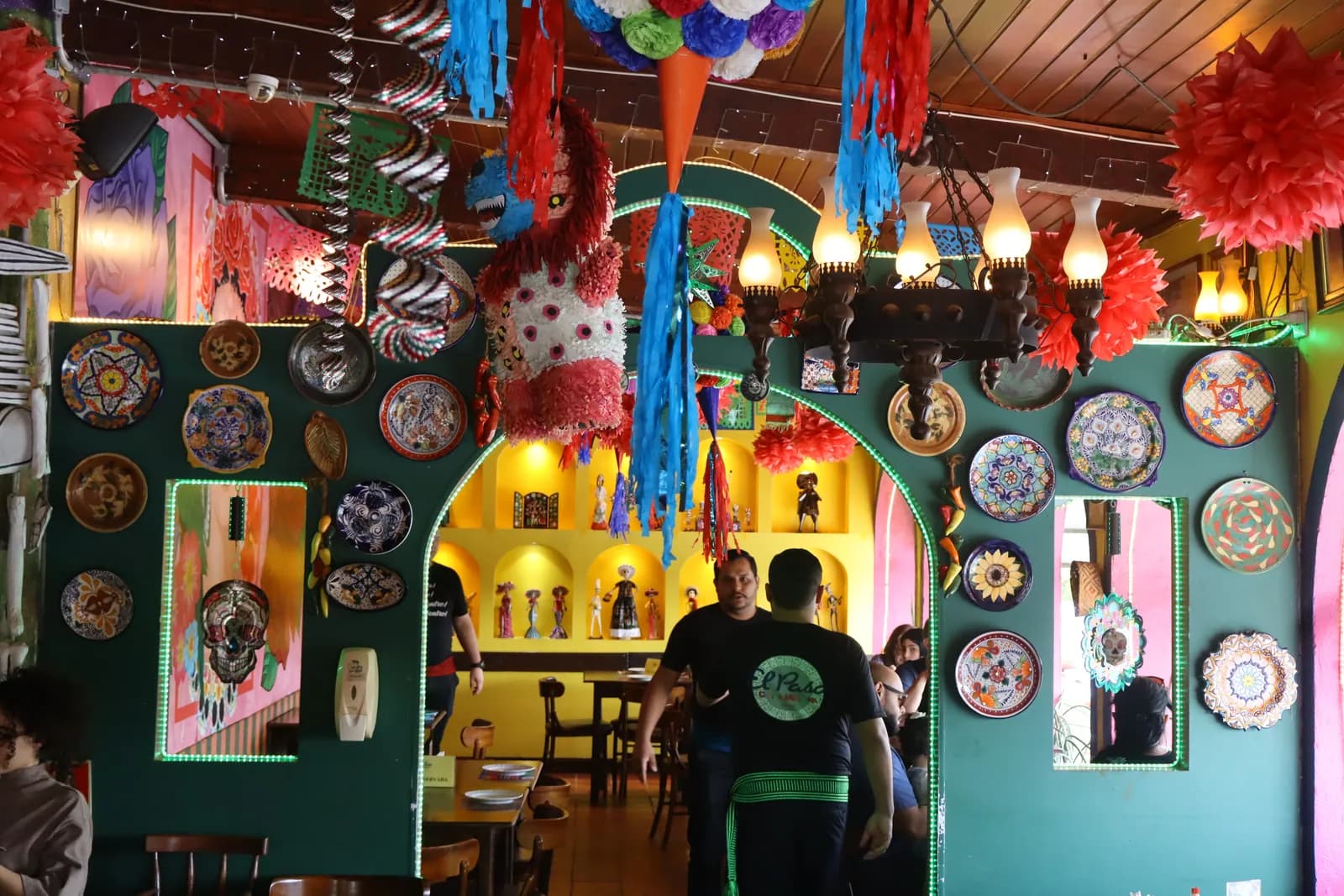 Arco com parede de pratos, nichos com bonecas, piñata e lustre
