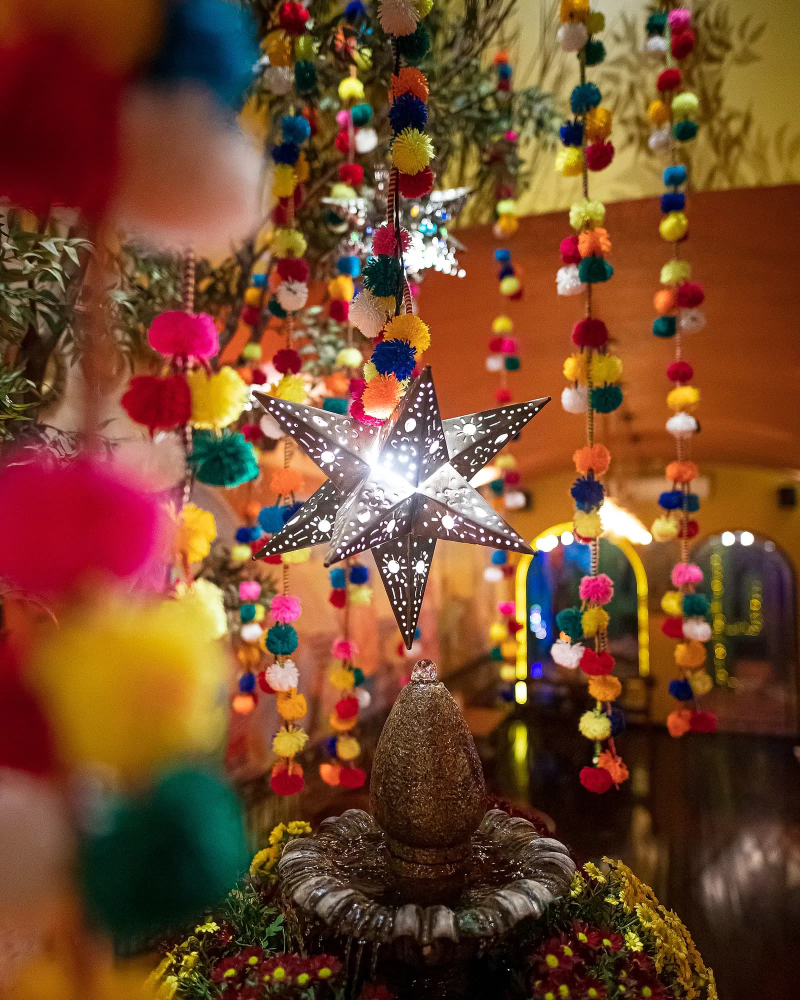 Estrela de lata mexicana iluminada entre fios de pompons coloridos sobre a fonte