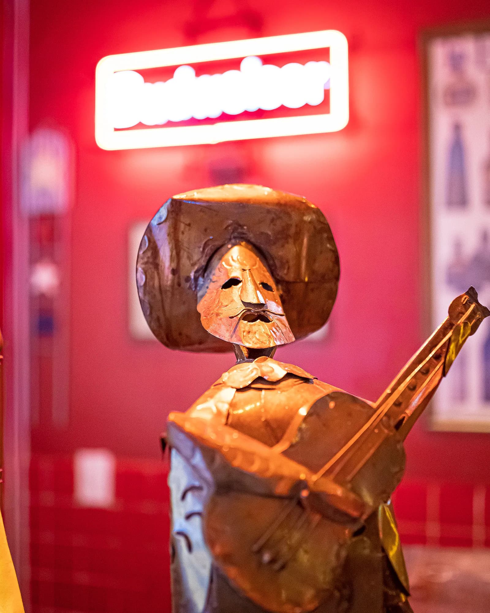 Escultura de mariachi em metal tocando violão diante de neon vermelho