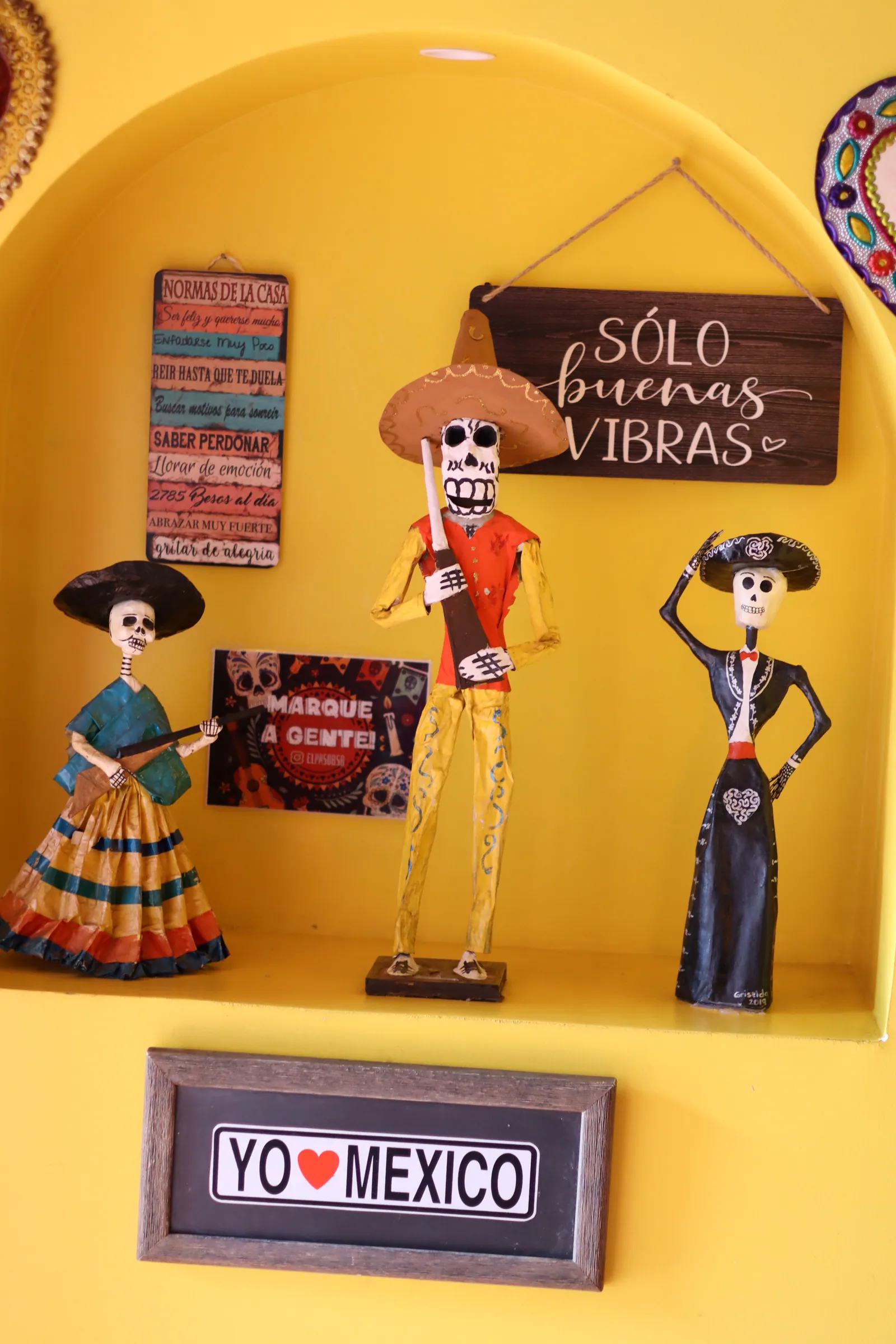 Nicho amarelo com catrinas de papel machê e a placa "Yo amo México"