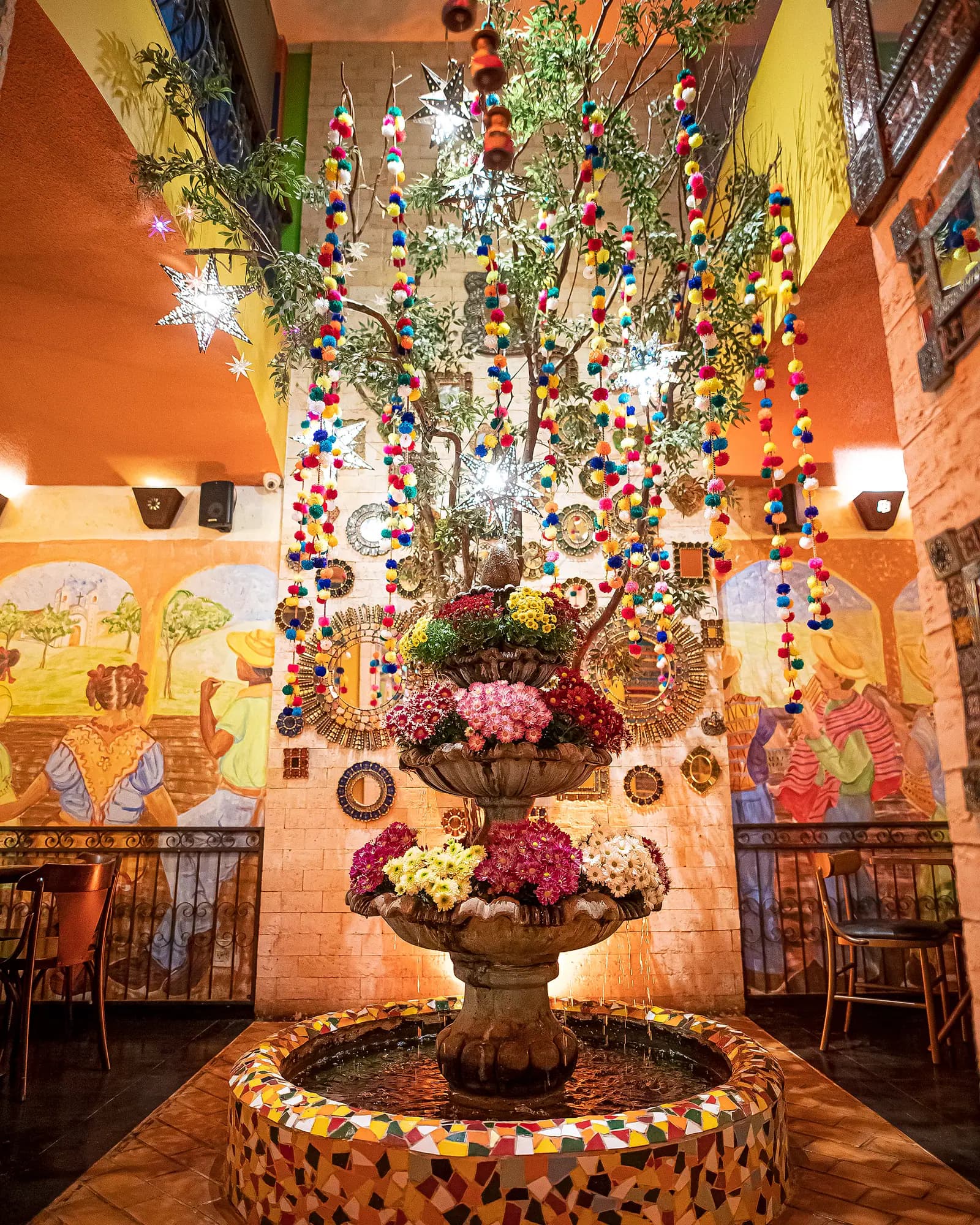 Fonte com flores entre murais mexicanos, espelhos artesanais e cascatas de pompons coloridos