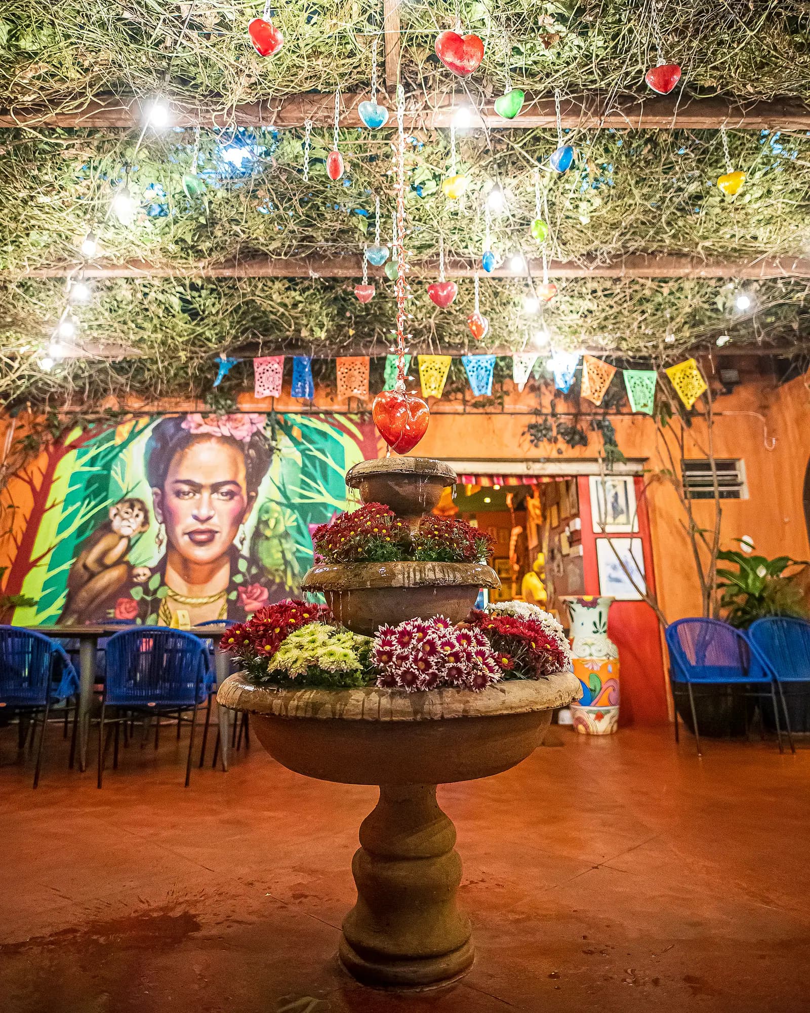 Pátio com fonte florida, corações de vidro pendurados e mural da Frida Kahlo ao fundo