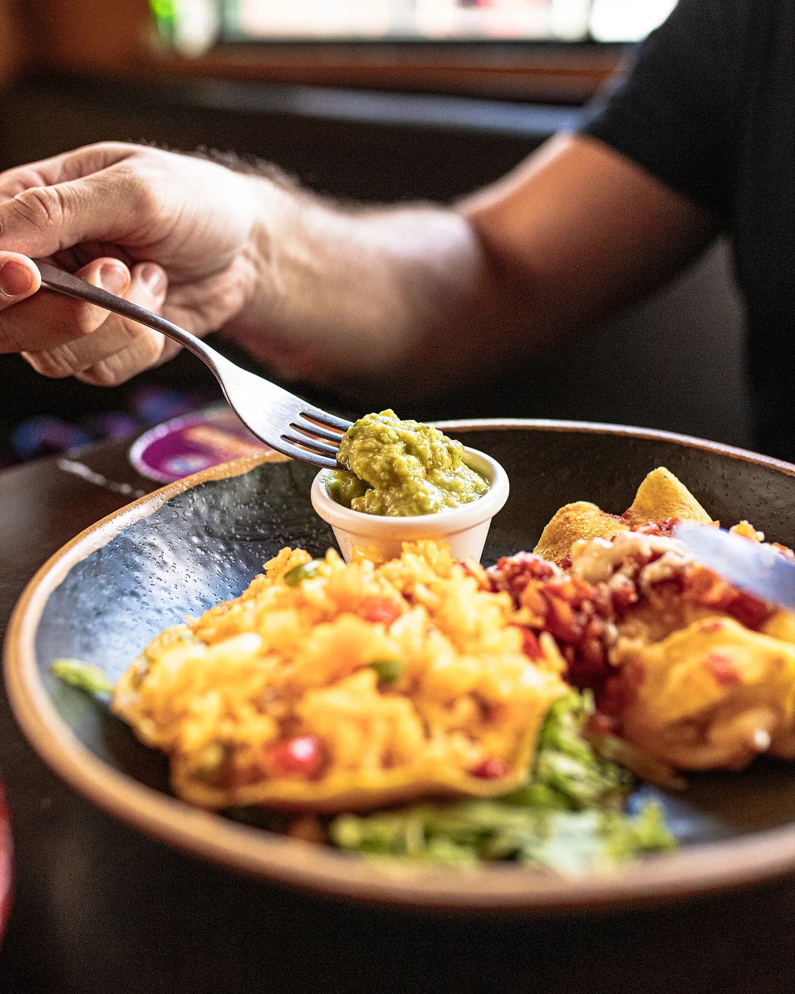 Garfo com guacamole sobre prato de enchiladas com arroz mexicano