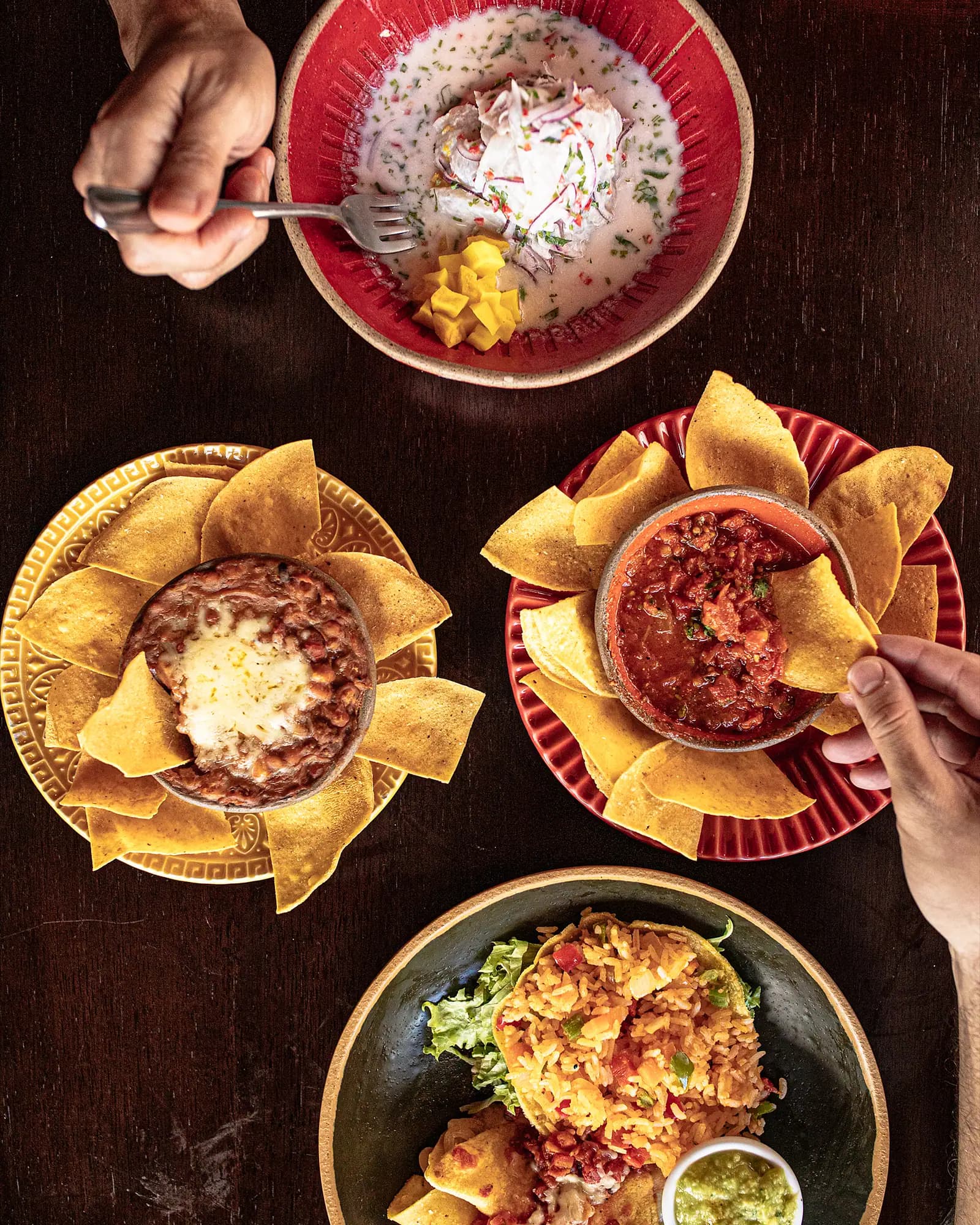 Mesa vista de cima com ceviche, frijoles com queijo, salsa roja e totopos