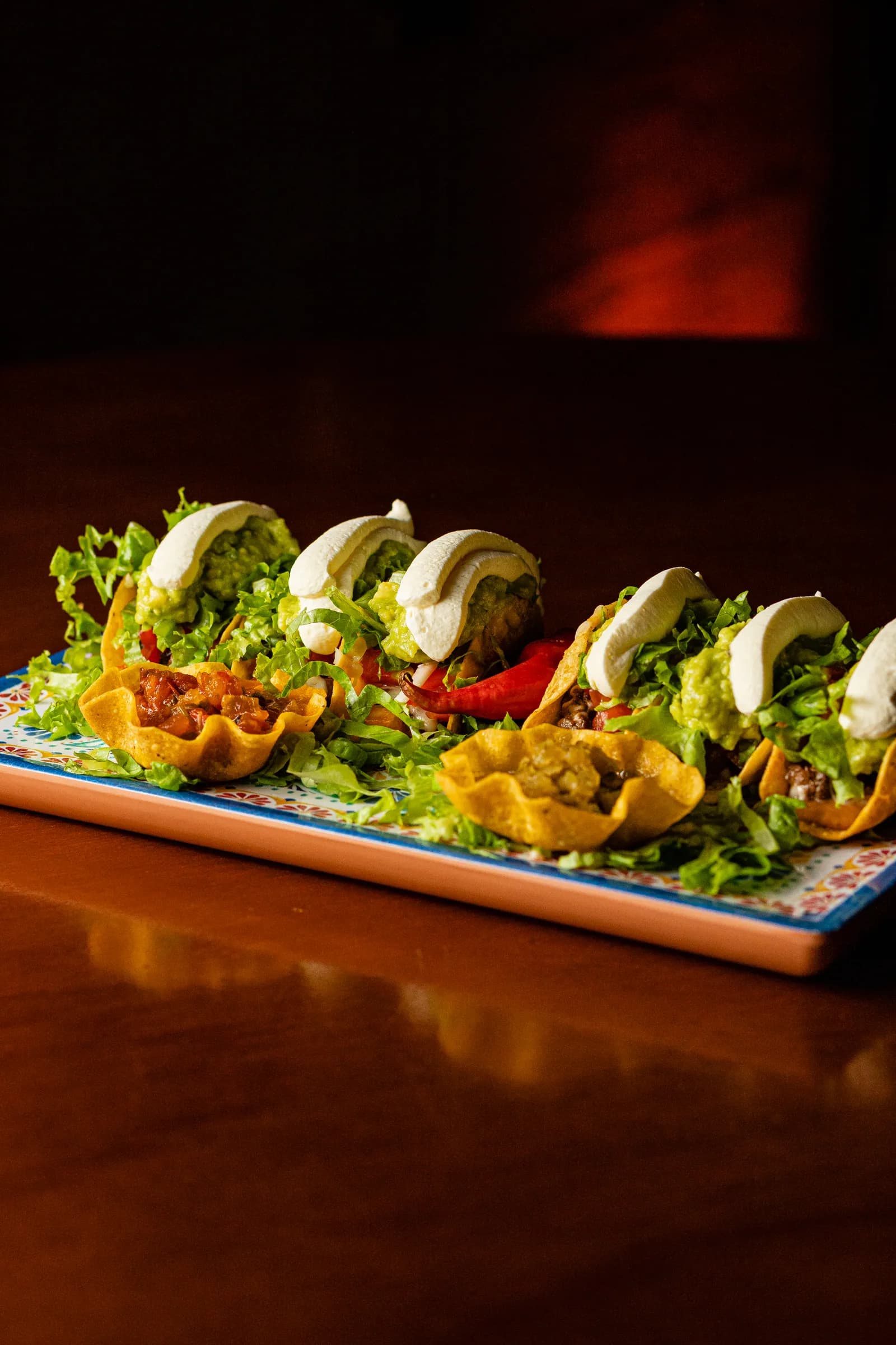 Travessa de tacos com alface, guacamole e sour cream sobre a mesa de madeira