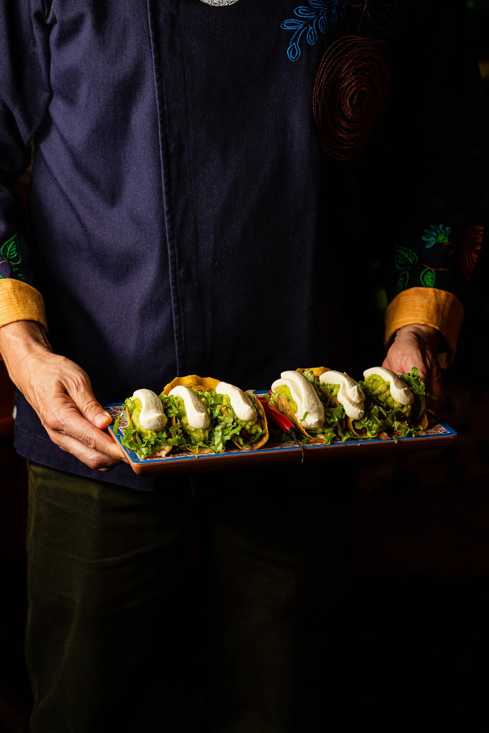 Chef segurando travessa de tacos com guacamole e sour cream