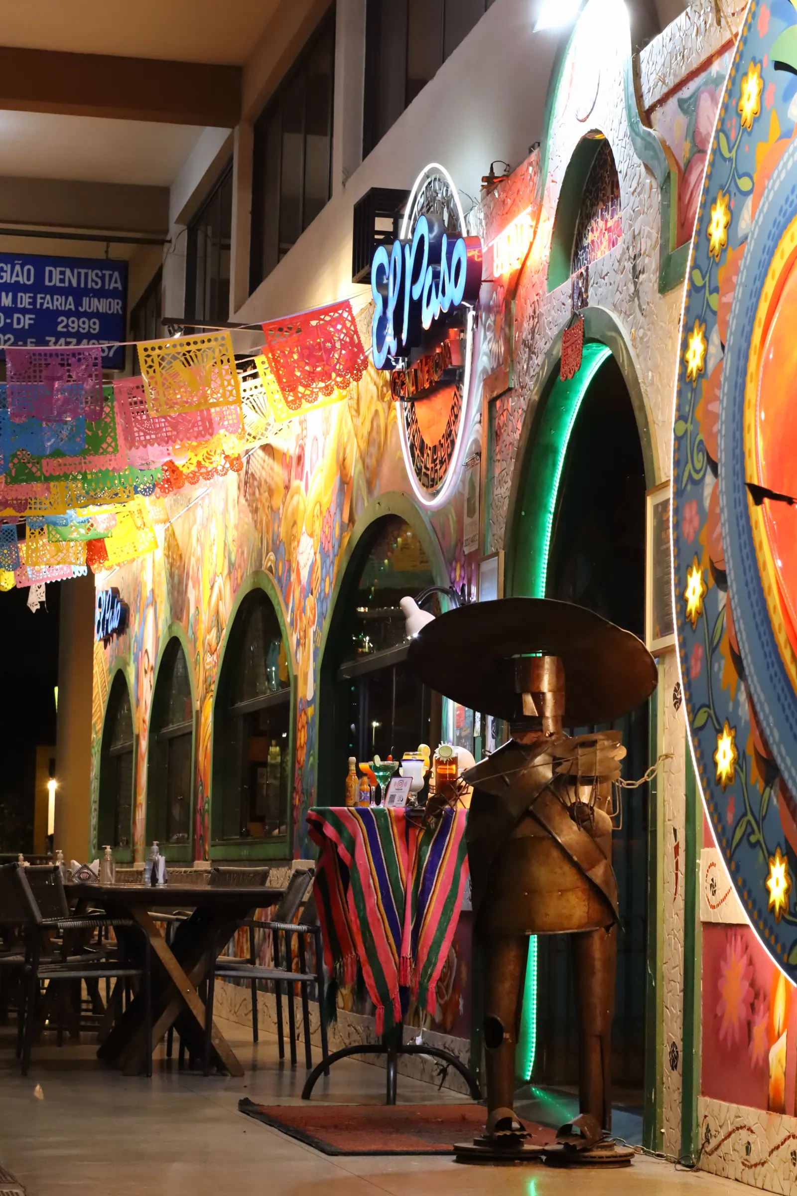 Fachada do El Paso Asa Norte à noite: letreiro luminoso, papel picado e mesas externas