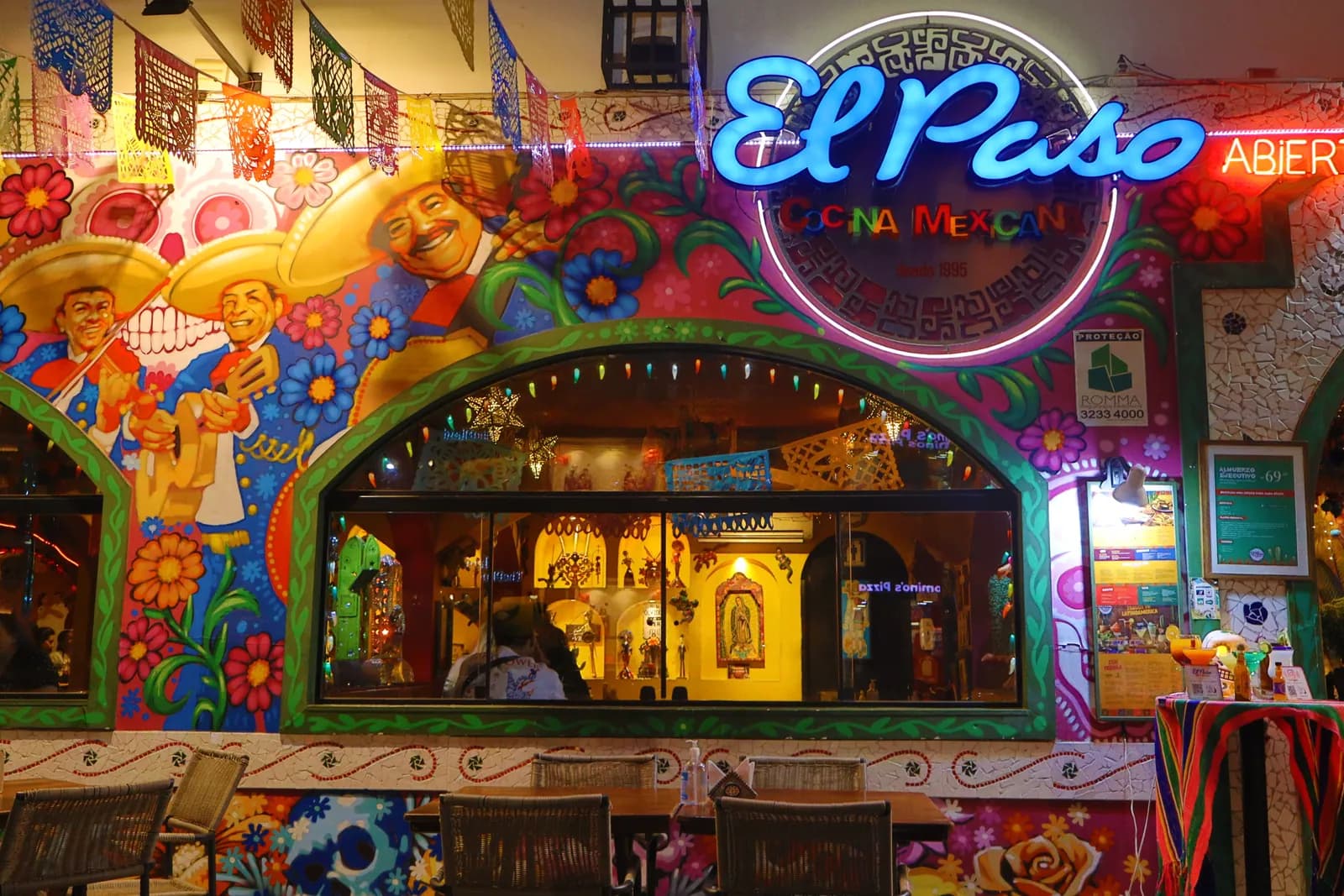 Entrada principal com letreiro iluminado, papel picado e vitrine decorada
