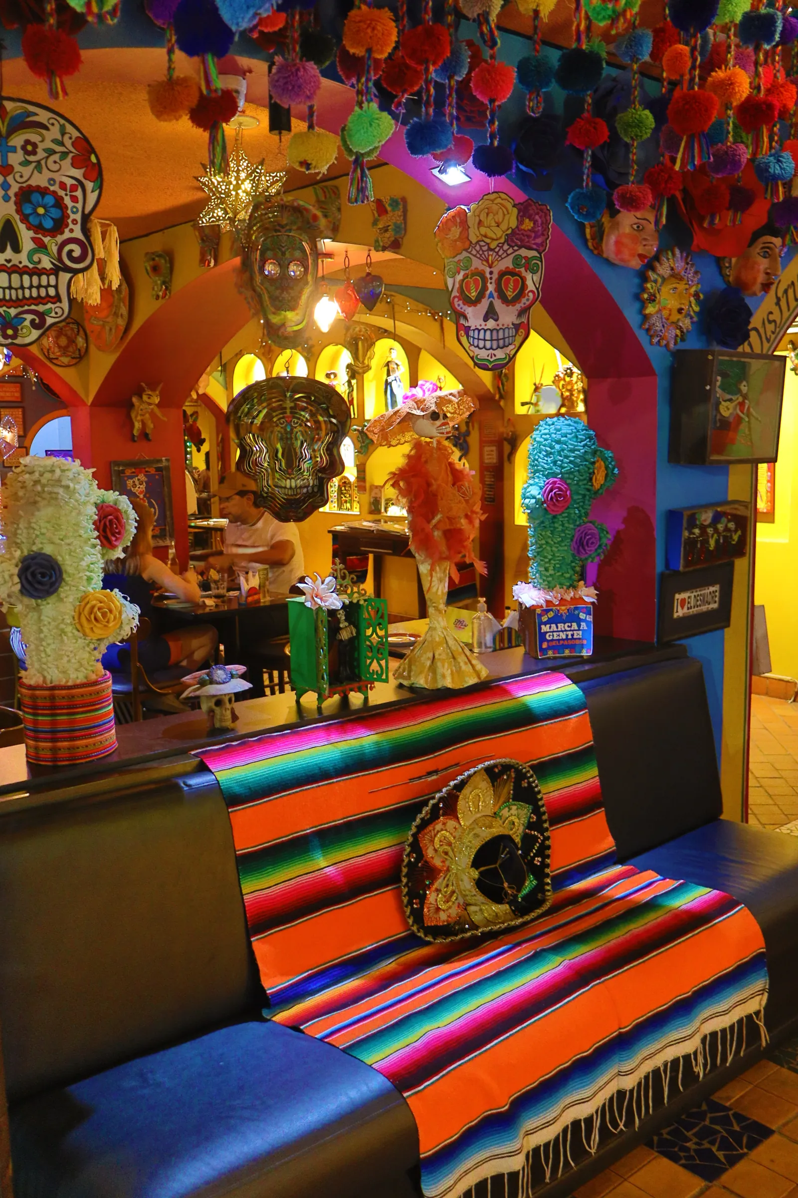 Salão com teto de pompons coloridos e vista do bar ao fundo
