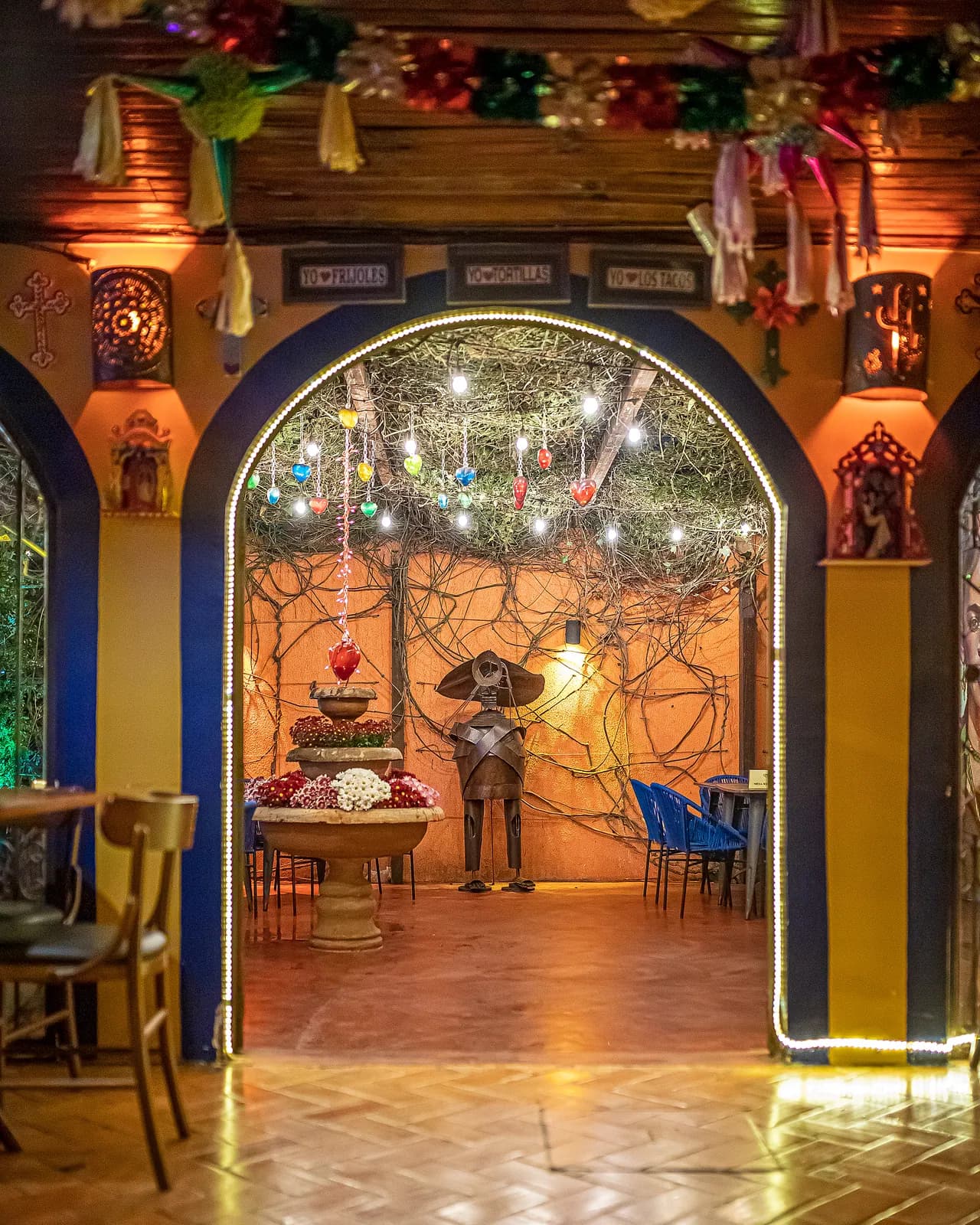 Arco azul e amarelo com cortina de luzes levando ao pátio da fonte